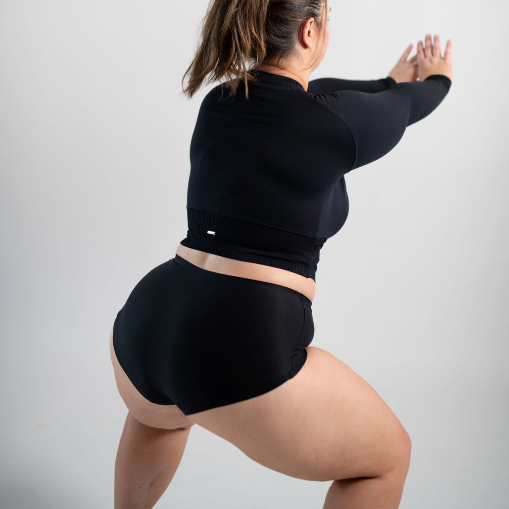 Woman wearing black seamless high rise Squaties and black top, squatting
